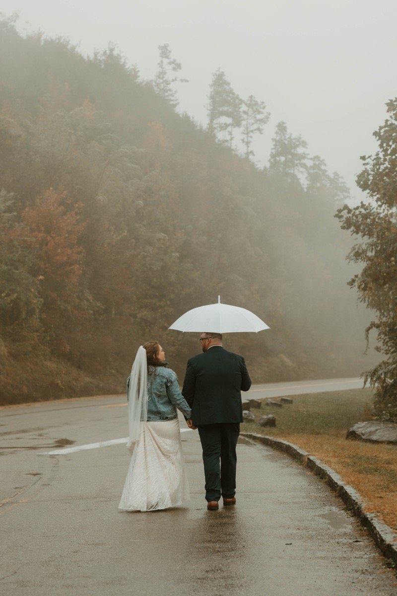 Bride and groom walking hand in hand through misty mountain road