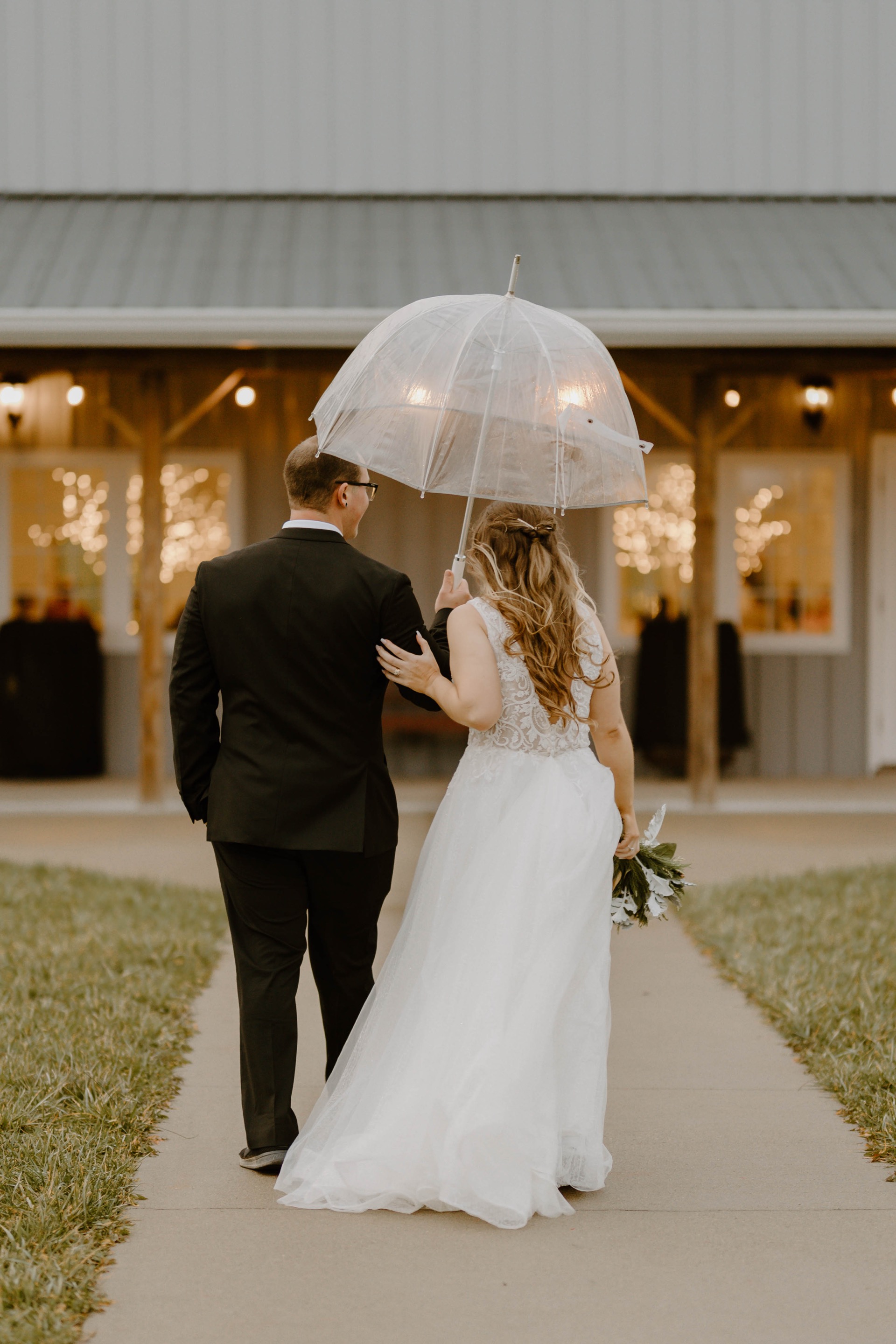 Bride and groom walking under a clear umbrella toward their wedding venue