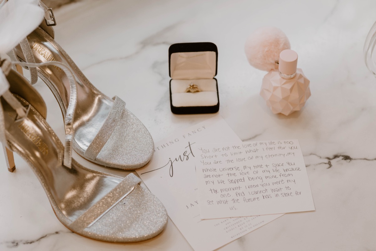Wedding vows, engagement ring, gold heels, and perfume on marble